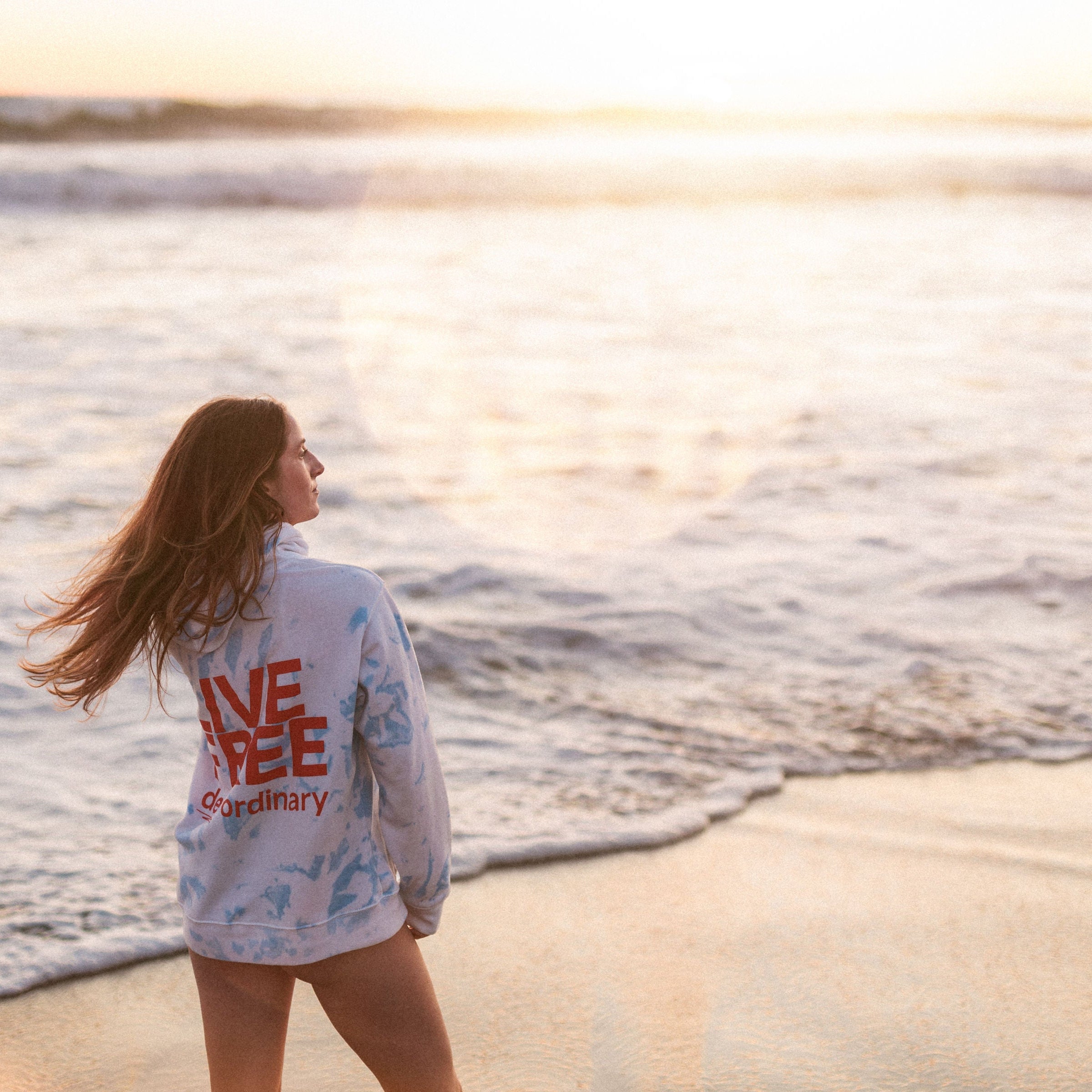 Woman standing on a beach with 'Live Free' shirt, sunset in the background