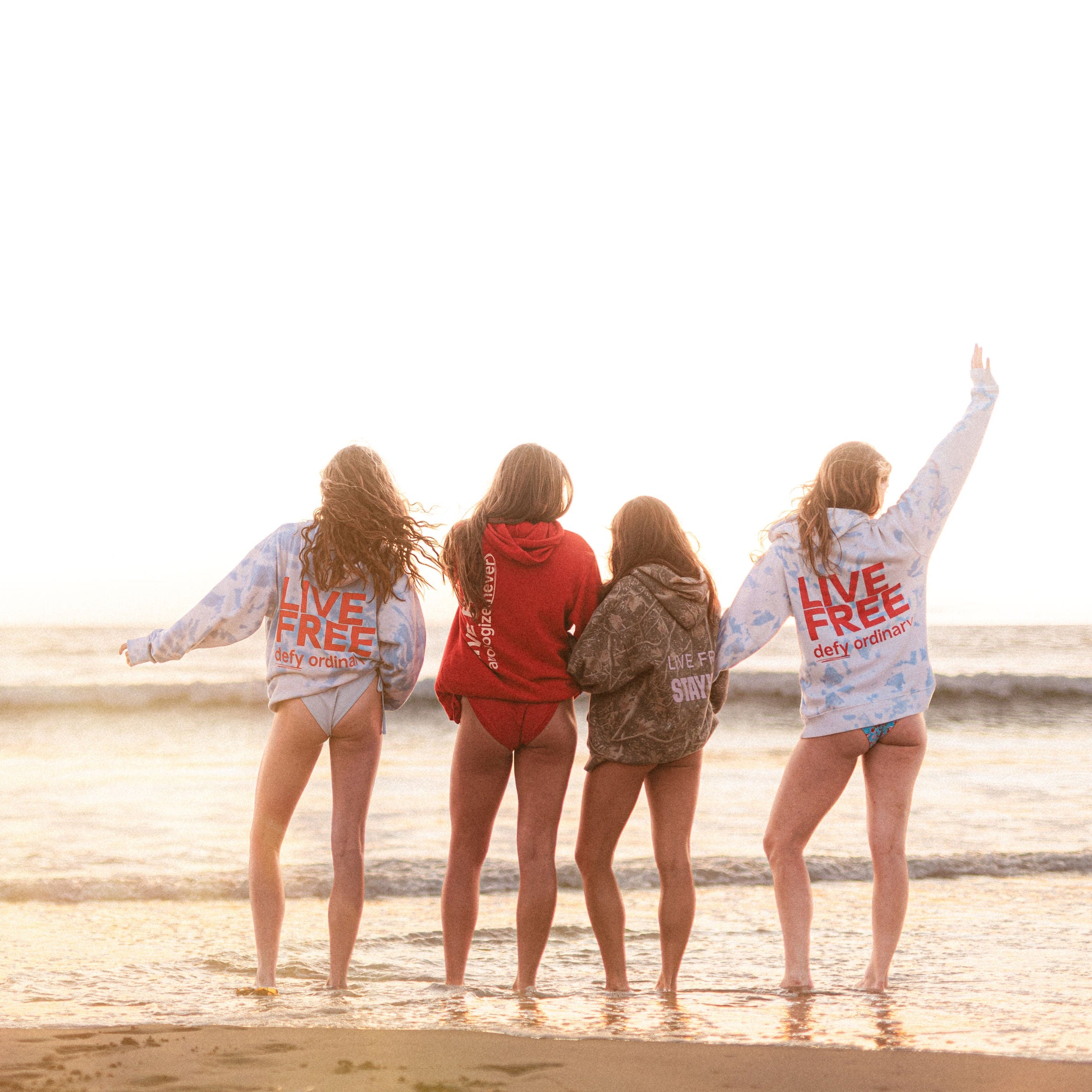 Four friends standing on a beach with 'Live Free' shirts.